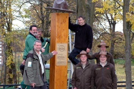 Mitarbeiter der Holzbauwerkstatt befestigen Rangerhut auf der 2,50 Meter hohen Holzstele